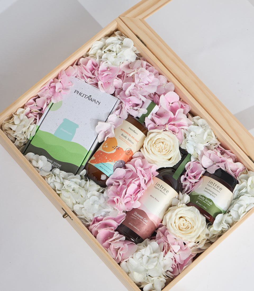 Luxury spa gift set in wooden box with pink and white hydrangeas, cream roses, and skincare products including moisturizer and body scrub.