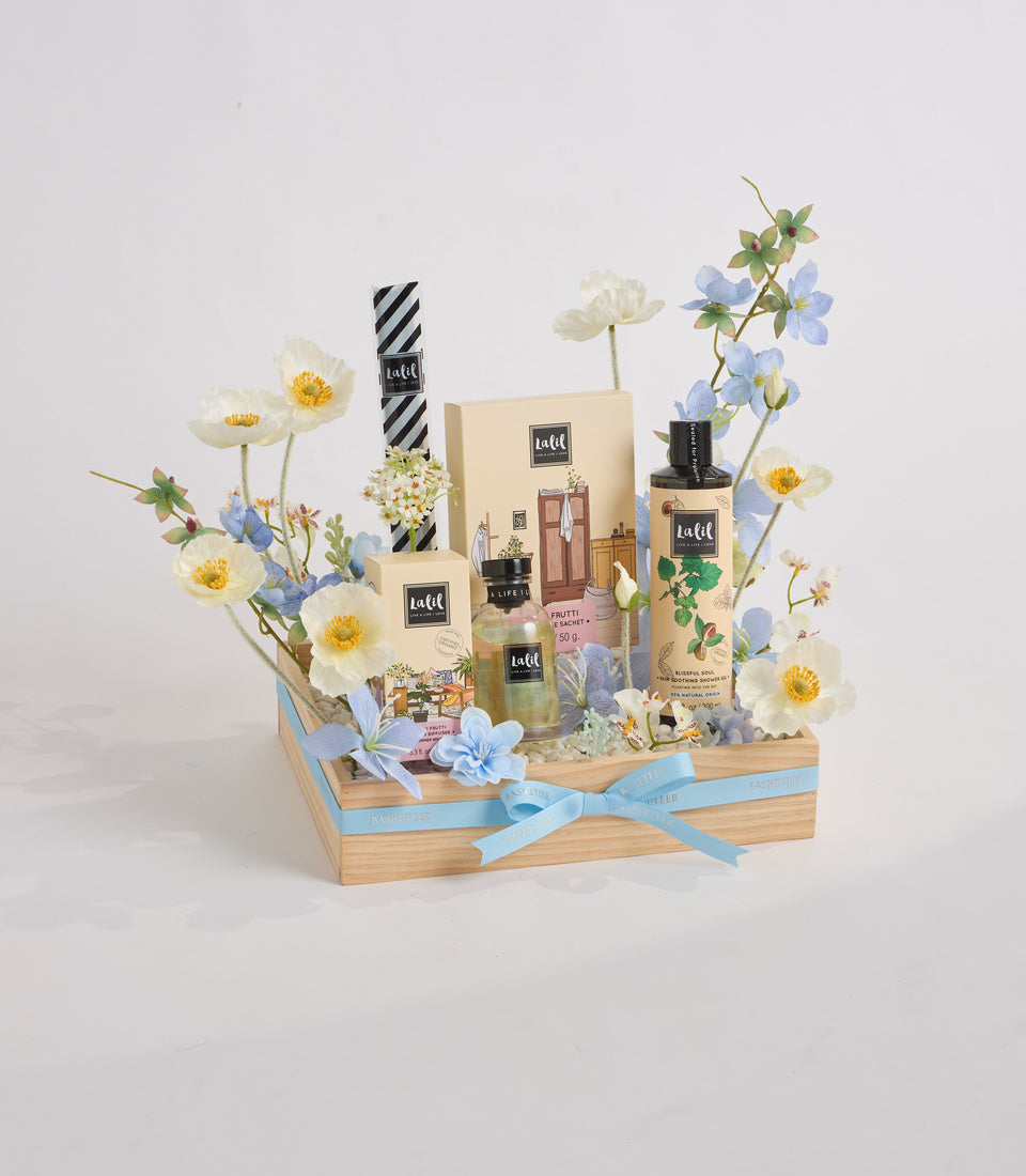 Wooden gift basket with white and blue flowers, luxury beauty products, striped black and white accents, and light blue ribbon bow on white background.