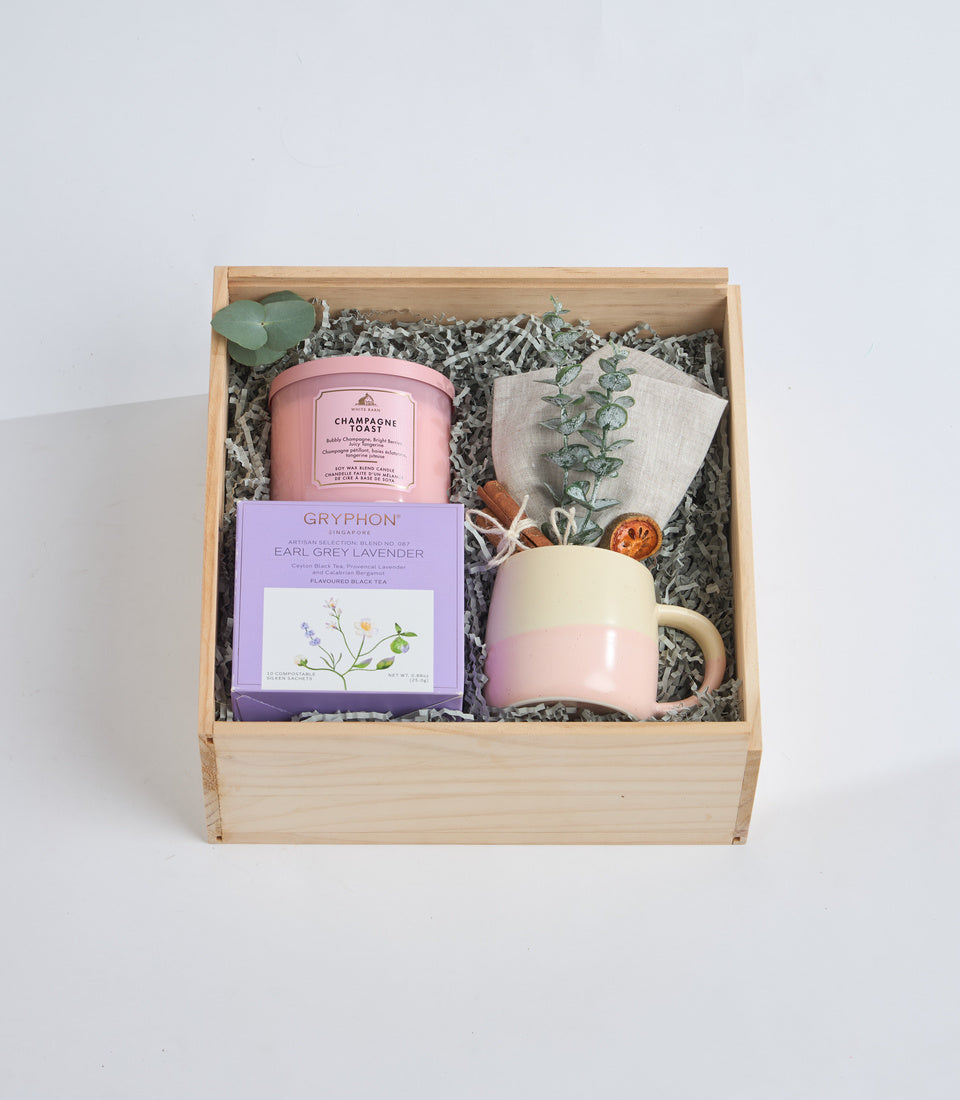 Wooden box gift set with pink candle jar, Gryphon Earl Grey Lavender tea box, cream mug, linen pouch, dried botanicals and shredded paper filler.
