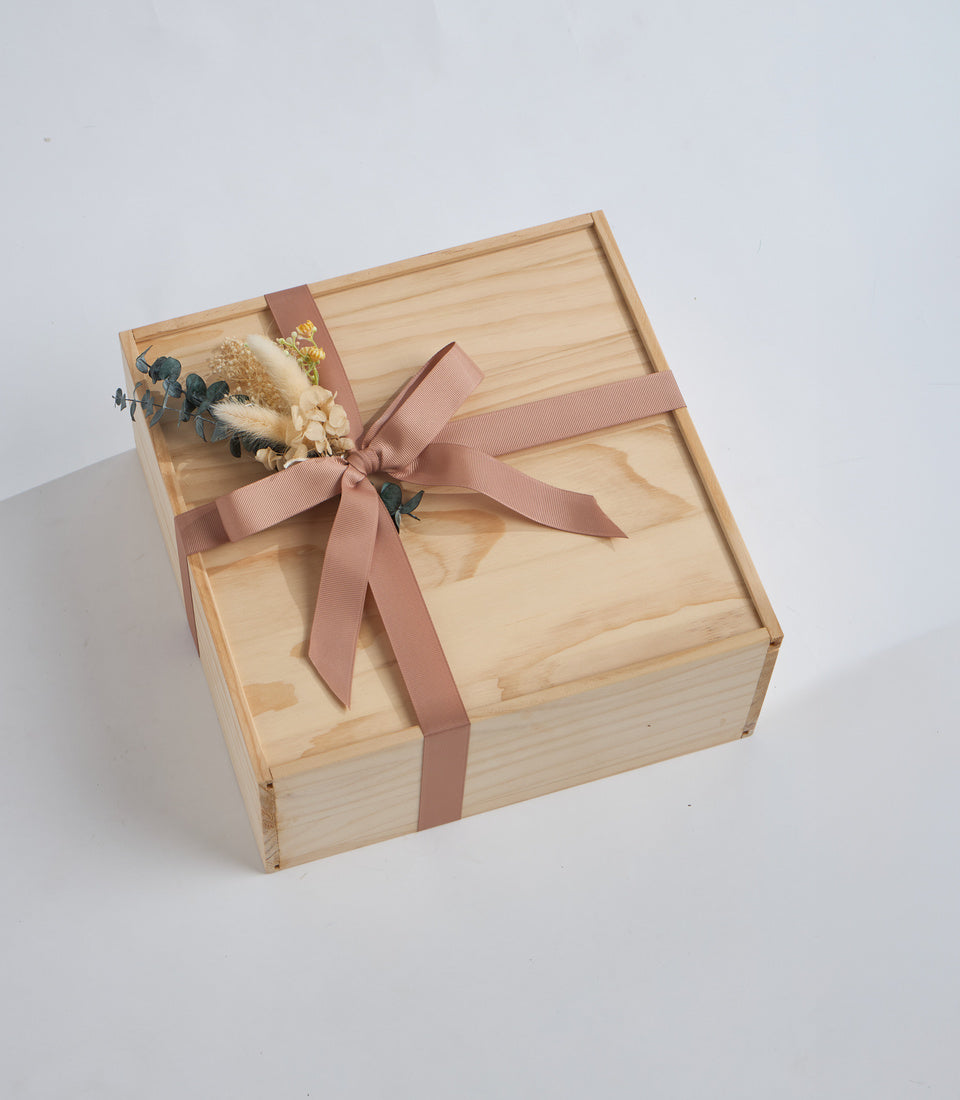 Wooden gift box with mauve ribbon bow and dried flower arrangement on lid, featuring eucalyptus and neutral-toned botanicals.