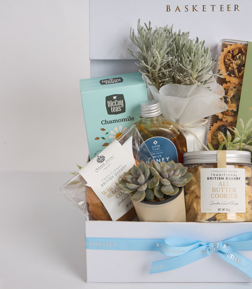 # Alt Text

Curated gift basket with succulents, chamomile tea, honey, cookies, and baked goods tied with light blue ribbon on white box.