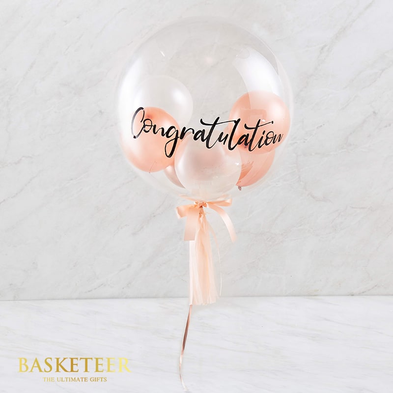 Clear bubble congratulations balloon with nested white, rose gold and pink balloons, tied with peach satin ribbon