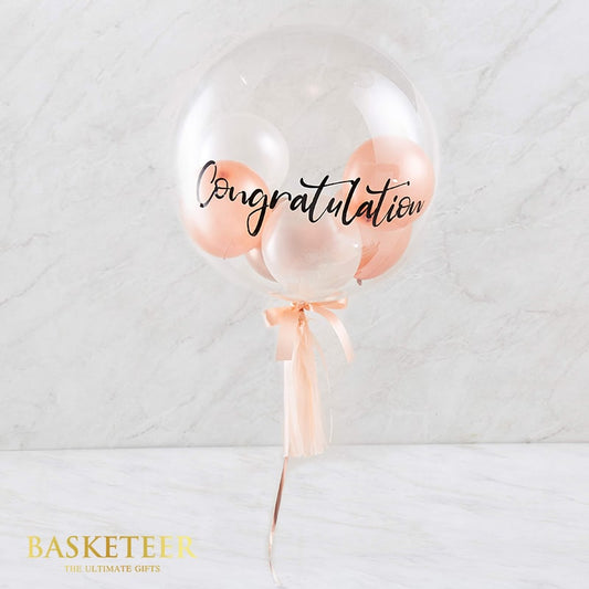 Clear bubble congratulations balloon with nested white, rose gold and pink balloons, tied with peach satin ribbon