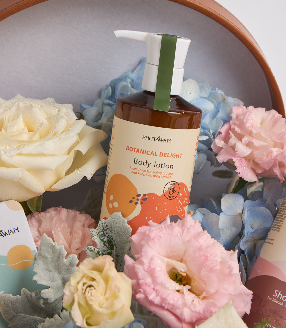 Phutawan Botanical Delight body lotion bottle with pump dispenser surrounded by fresh pink, white, and blue flowers in wooden bowl.