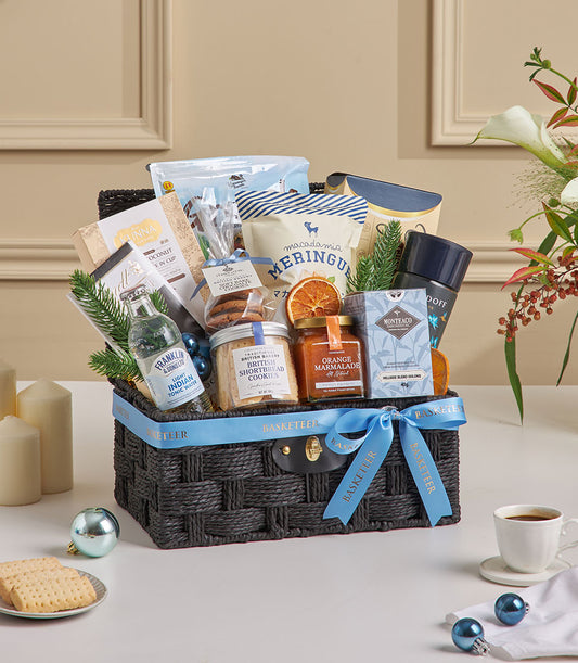 Luxury grey woven gift basket with blue ribbon containing gourmet granola, premium oolong tea, shortbread cookies, and