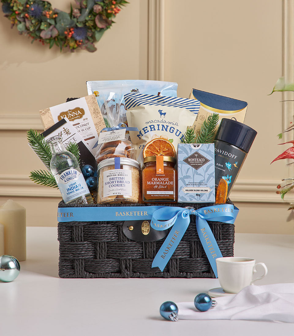Dark woven basket with blue ribbon filled with granola, tea, shortbread, and gourmet treats for New Year gifting