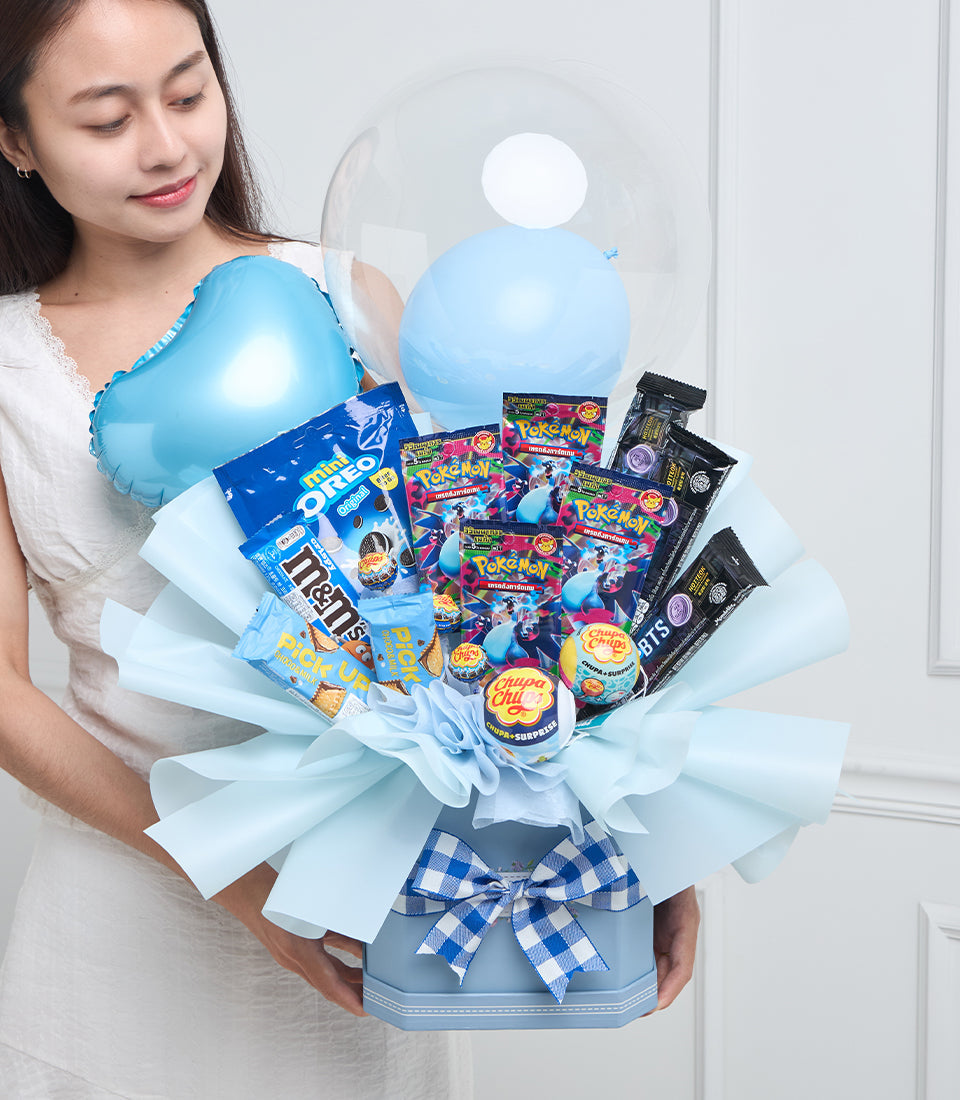 Blue balloon bouquet gift arrangement with Pokémon cards, candies, and BTS merchandise wrapped in light blue tissue paper with checkered ribbon bow.