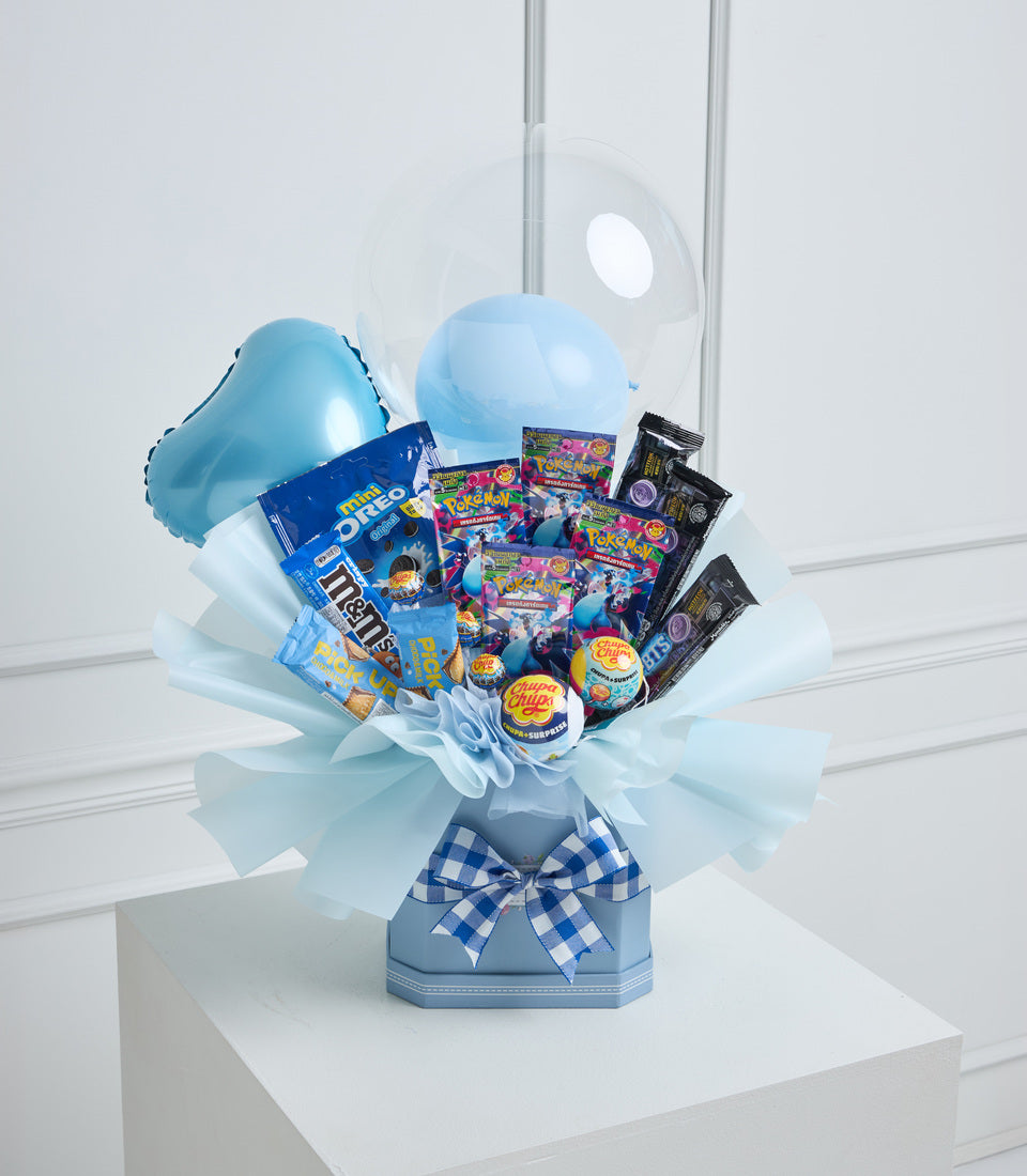 Blue candy bouquet with inflatable balloons, wrapped in tulle with checkered bow, containing assorted sweets and snacks on white pedestal.