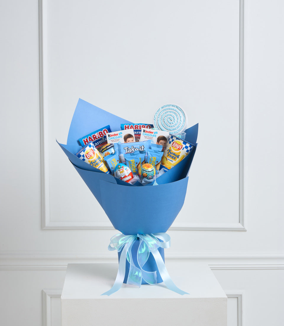 Blue wrapped snack bouquet with candy, chips, and chocolate treats tied with light blue ribbons, displayed against white paneled background.