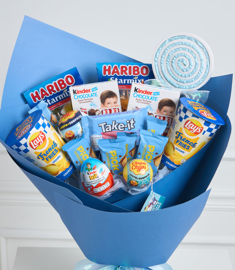 Blue gift basket overflowing with assorted candies, chocolates, and snacks including Haribo, Kinder, Lay's, and Chupa Chups brands.