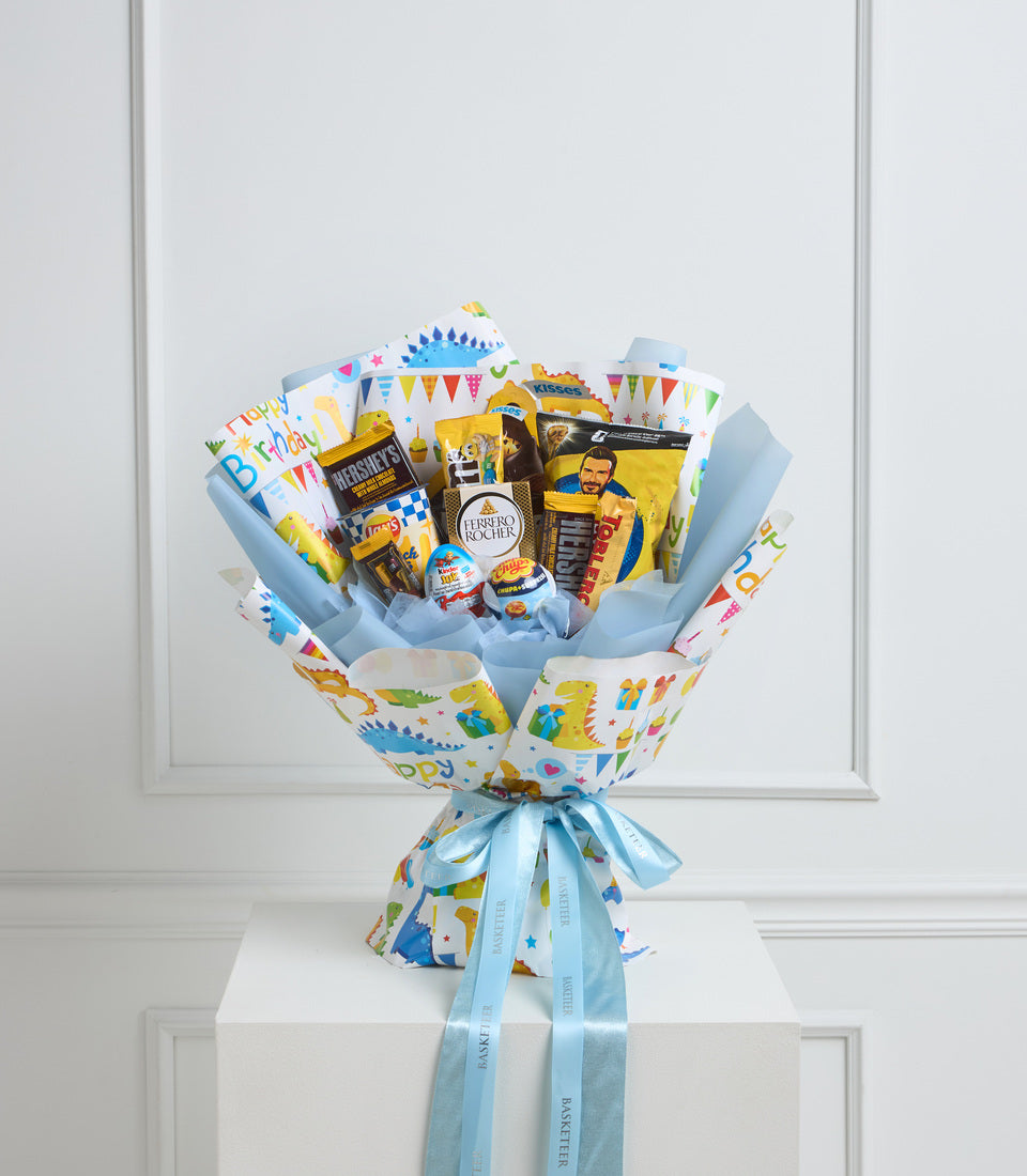Colorful birthday gift bouquet with blue and white patterned wrapping, filled with chocolates, snacks, and treats, tied with light blue ribbons.