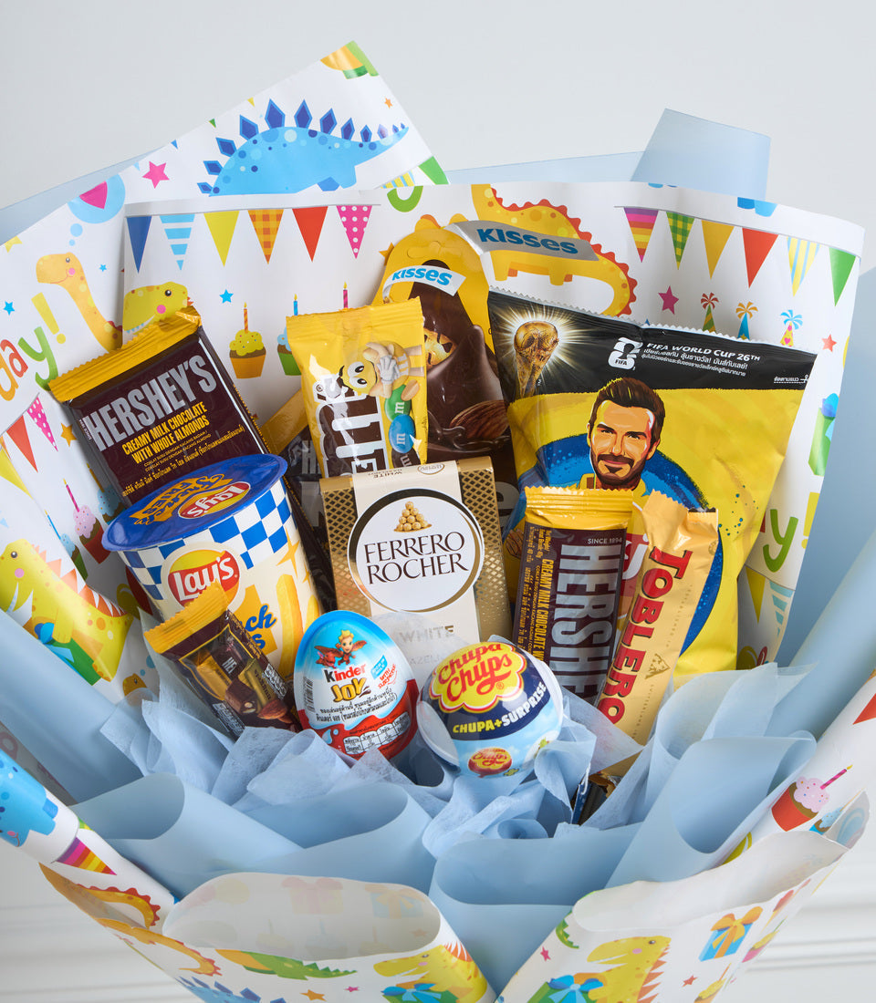 Colorful gift basket with dinosaur-themed wrapping paper containing chocolates, snacks, candy, and FIFA merchandise in yellow and blue tones.