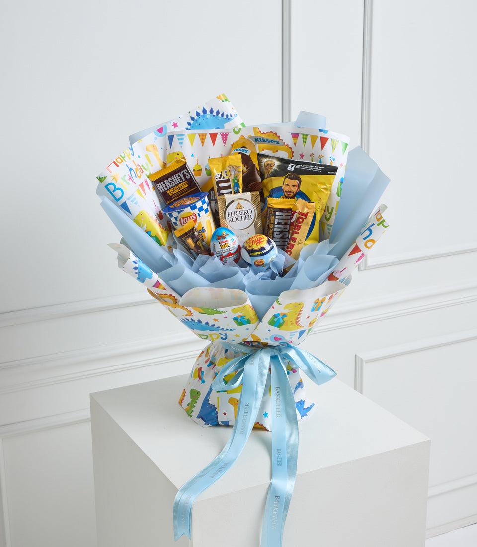Colorful celebration gift bouquet with snacks and chocolates wrapped in blue and yellow festive paper, tied with light blue ribbon bow.