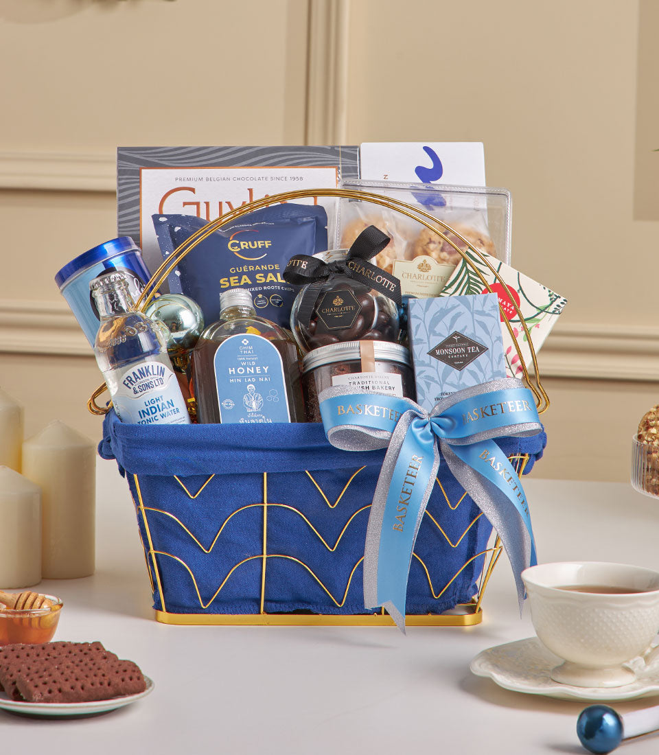 Midnight blue luxury gift hamper with Belgian chocolate, gourmet teas, and artisan treats in wire basket with gold accents