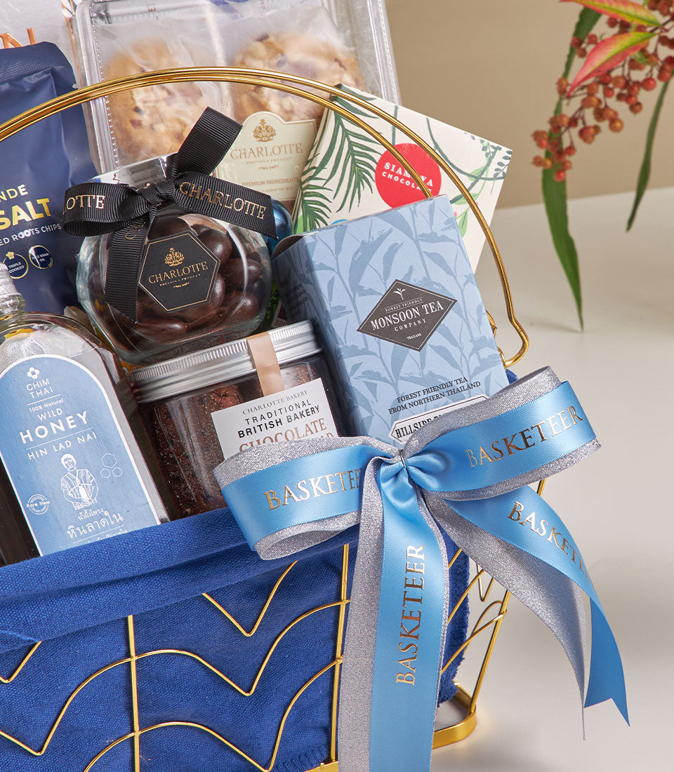 Midnight blue luxury hamper with gourmet chocolates, honey, tea, and artisan cookies in gold wire basket