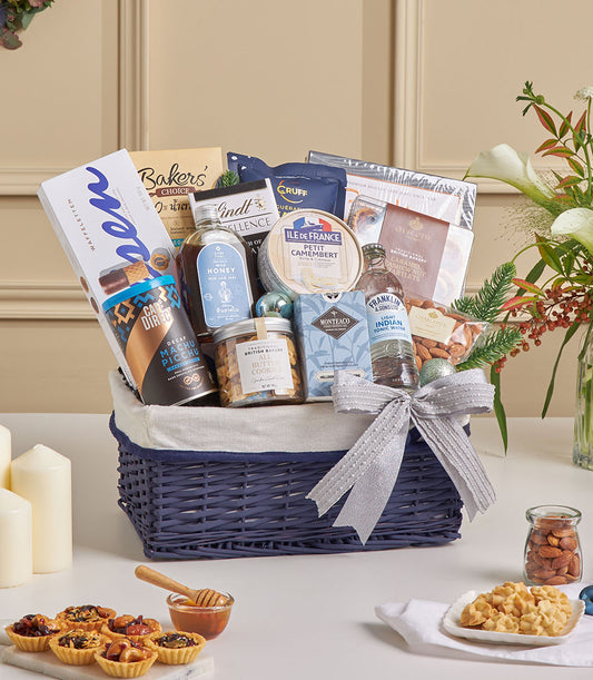 Dark blue wicker hamper with sea salt dark chocolate, Camembert cheese, gourmet treats, and silver ribbon for New Year