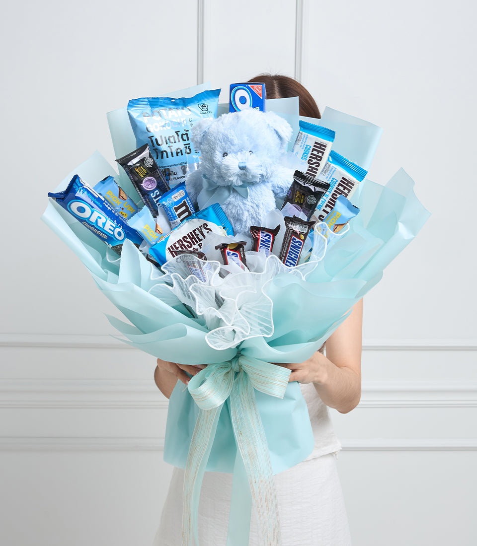 # Alt Text

Light blue wrapped candy bouquet with white teddy bear, chocolates, cookies, and snacks arranged with white tulle and ribbon bow.