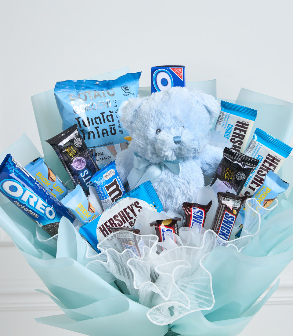 Light blue wrapped gift bouquet with white fluffy teddy bear, assorted snacks including Oreo, Hershey's, and chocolate bars, arranged with sheer white and blue ribbons.