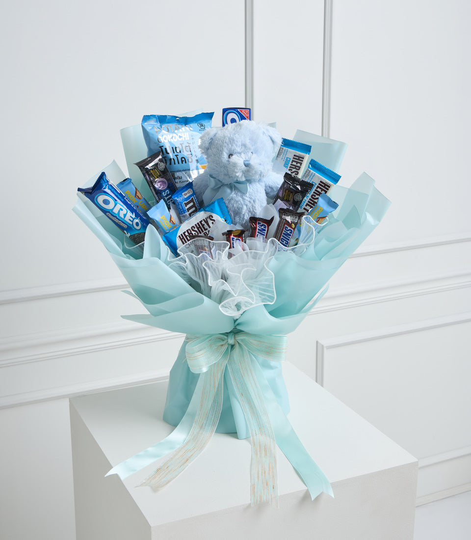 Light blue wrapped bouquet with assorted chocolates, candies, snacks, and a white stuffed teddy bear, tied with ribbon bow.