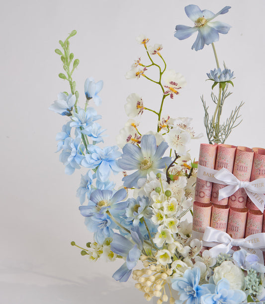Elegant floral gift arrangement with blue and white flowers, cream orchids, and red decorative boxes tied with white ribbons against a neutral background.