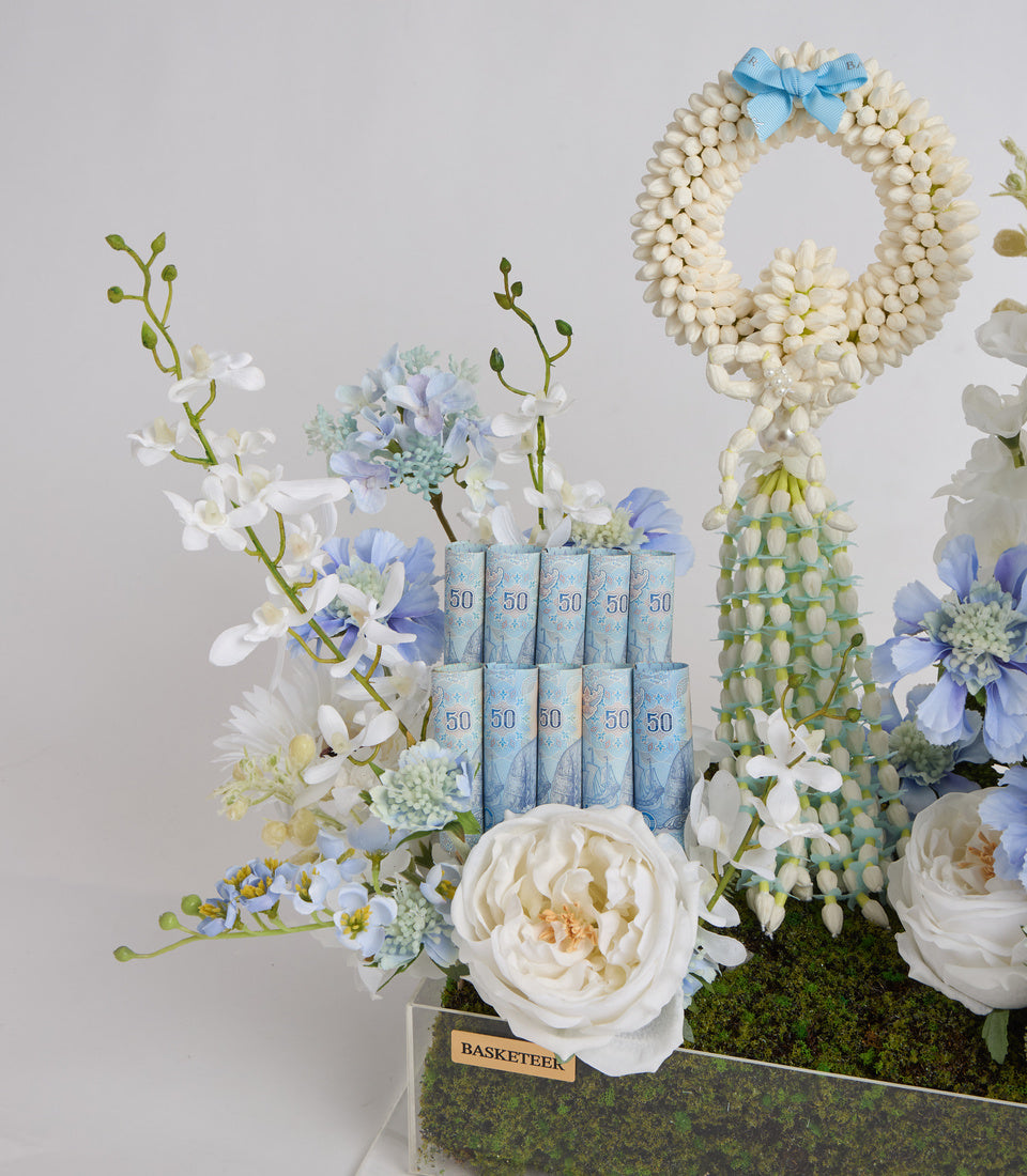Elegant floral arrangement with white peonies, blue flowers, and greenery in moss-lined basket with pearl wreath and blue tissue boxes marked "50".