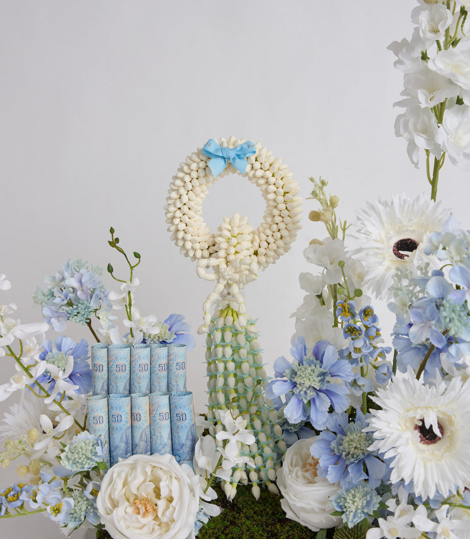 Luxurious gift set with cream pearl beaded wreath, blue ribbon bow, blue SPF 50 sunscreen tubes, green cacti, and white and blue fresh flowers.