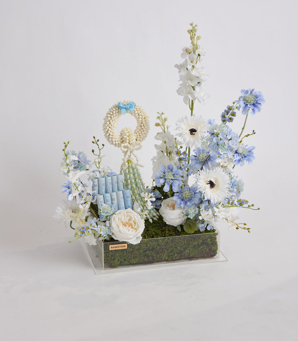 Luxe floral arrangement featuring white roses, blue daisies, and delicate white flowers with decorative elements in a modern rectangular container with moss base.