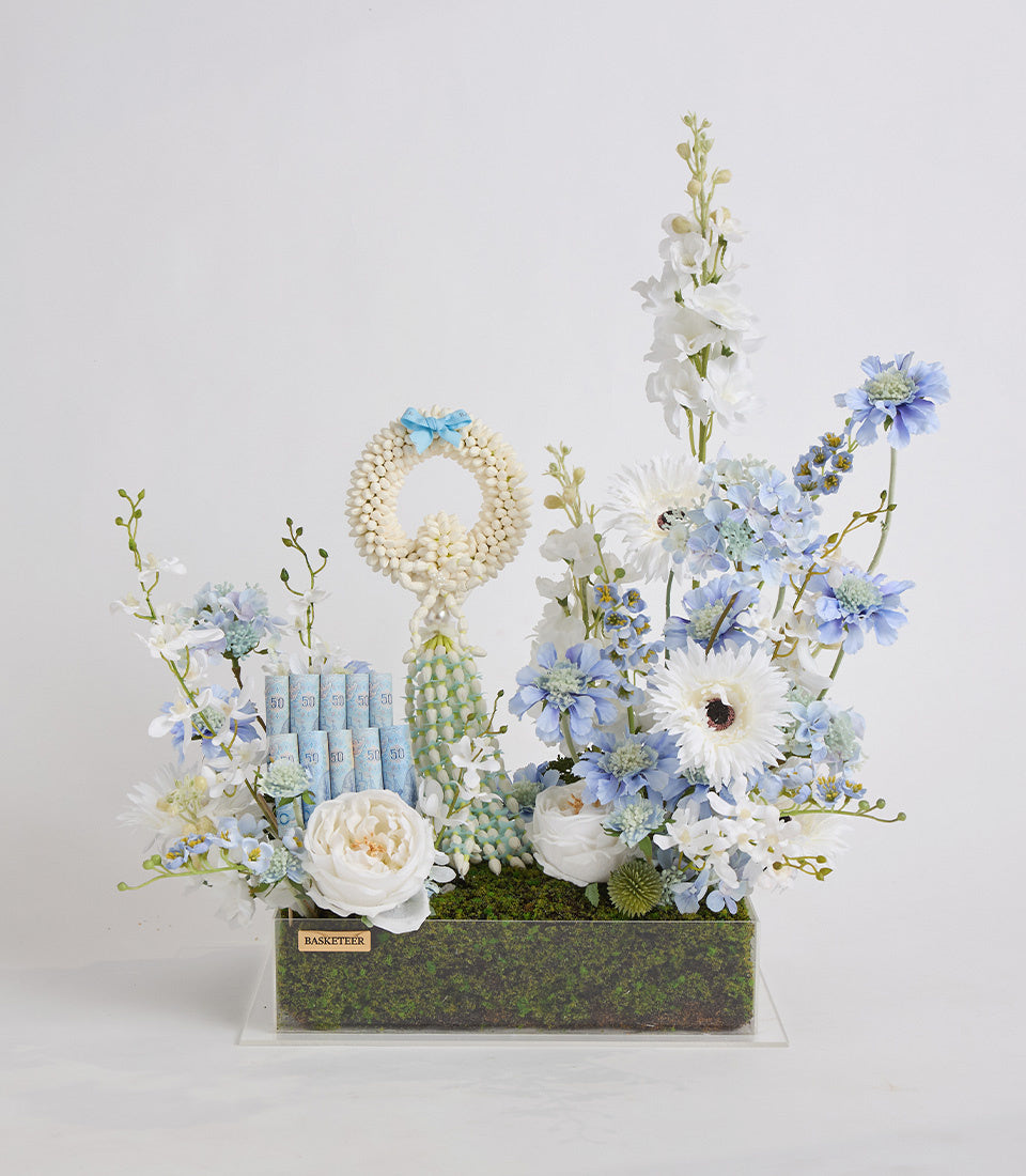 Elegant floral arrangement with blue and white flowers, pearl beads, decorative cactus, and green moss in a textured container, luxury gift style.