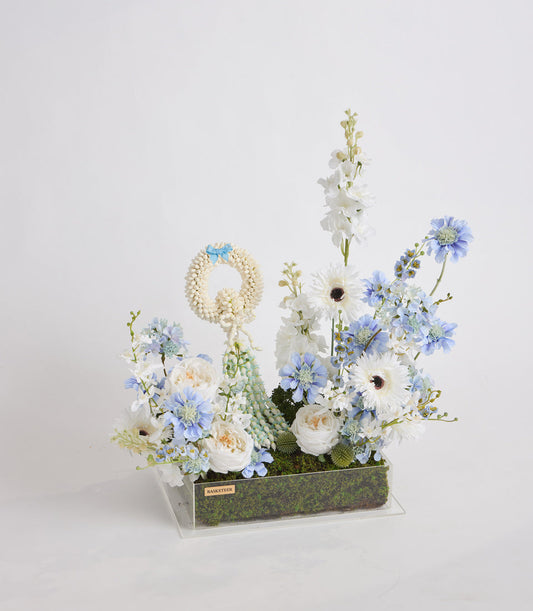 Floral arrangement with white gerberas and roses, blue cornflowers, white delphiniums in clear acrylic box with moss base and gold nameplate.