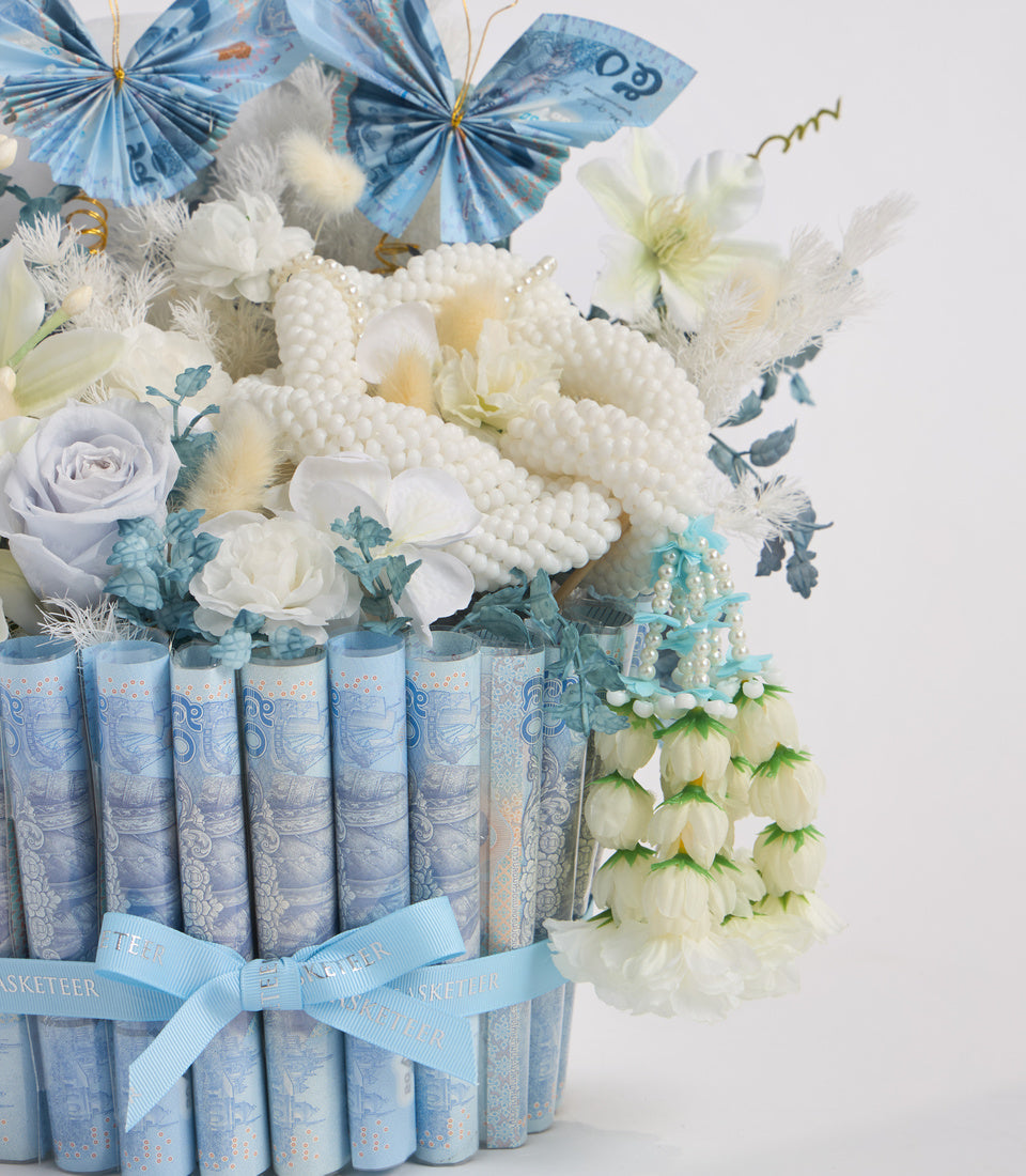 Luxury floral arrangement with white roses and cream flowers in blue patterned book-wrapped vase, topped with decorative paper butterflies and pearl beads.