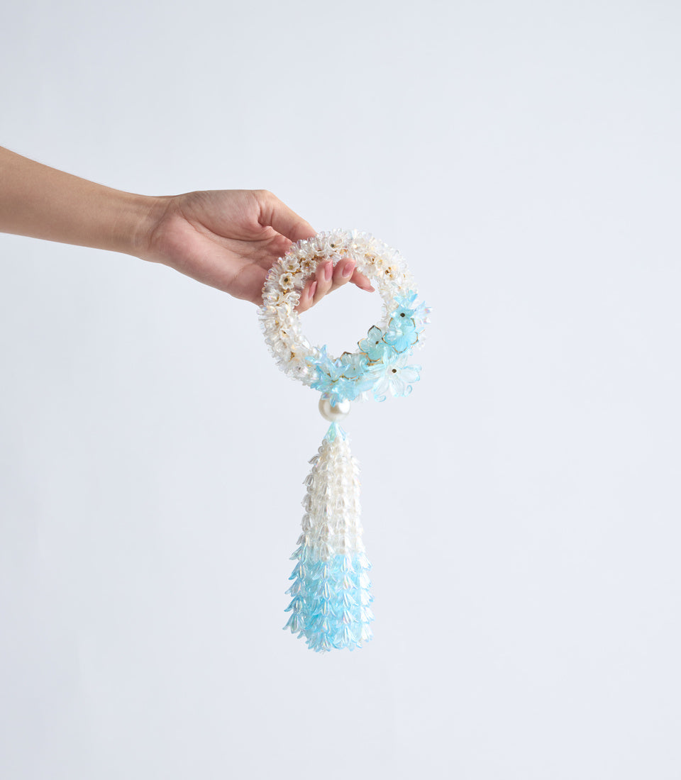 Hand holding beaded bracelet with tassel. White and light blue beaded circular band with matching ombre blue teardrop tassel.