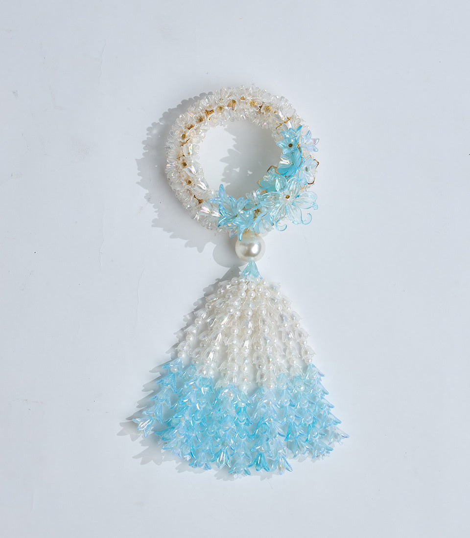 Beaded tassel ornament with clear and turquoise glass beads, pearl accent, and loop closure on white background.