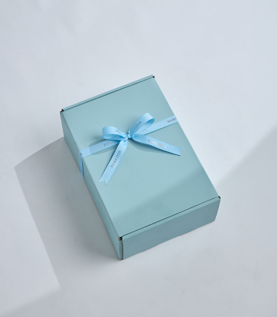 Light blue luxury gift box with pale blue ribbon bow, shot from above on white background with soft shadow.