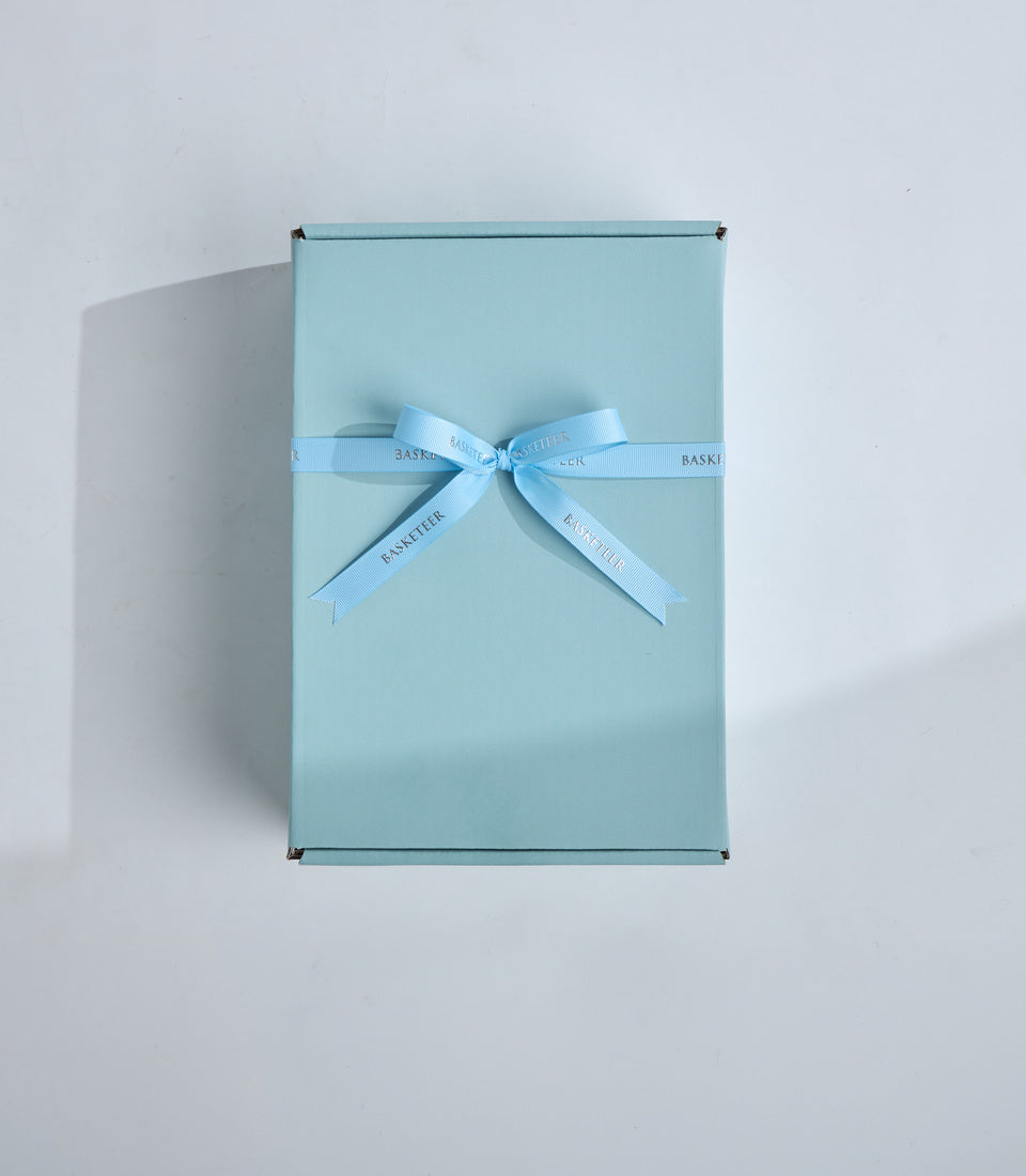 Light blue gift box with matching ribbon bow featuring "Baskeri" branding, photographed flat lay against white background.