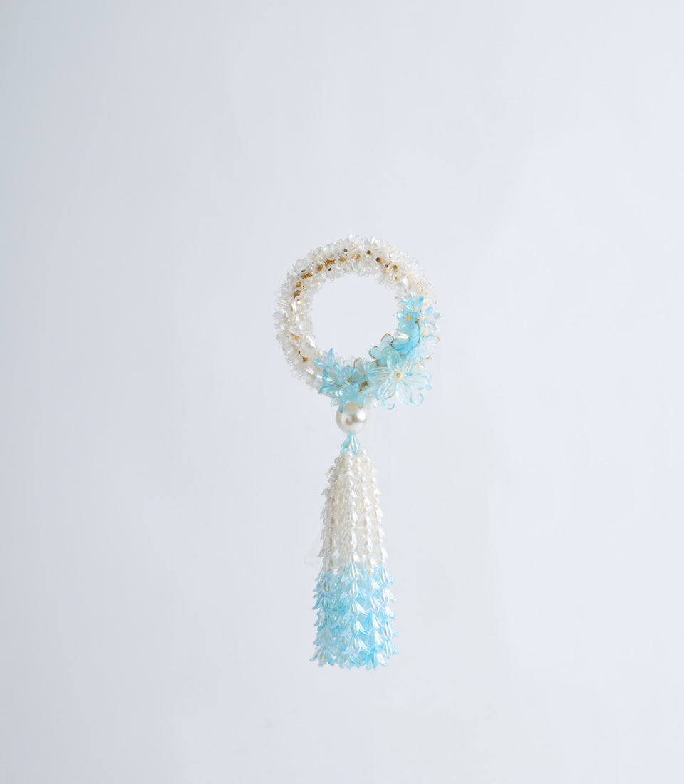 Beaded bracelet with white and gold beads forming a loop, turquoise flower accents, and a dangling tassel with white and blue beaded fringe.