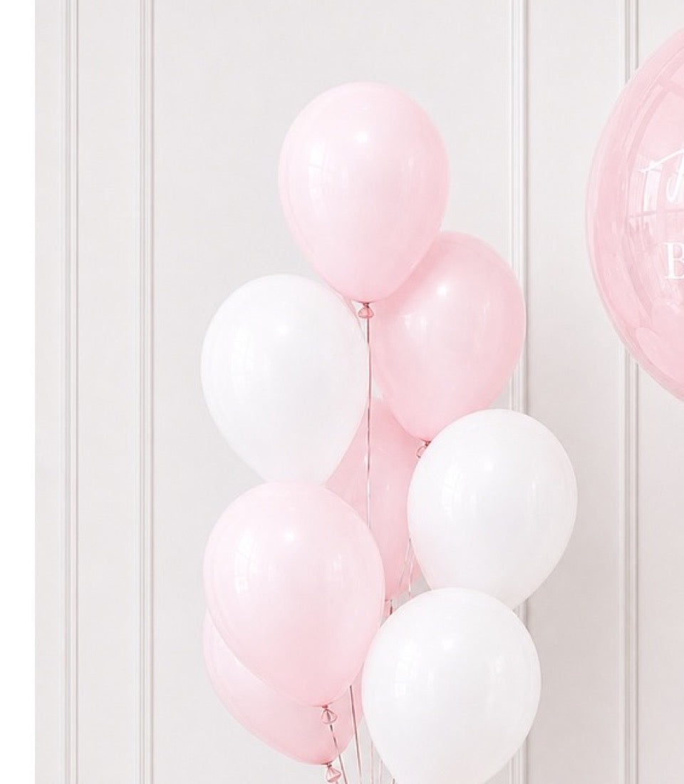 Pink and white latex balloons clustered together with strings against a white paneled wall background.