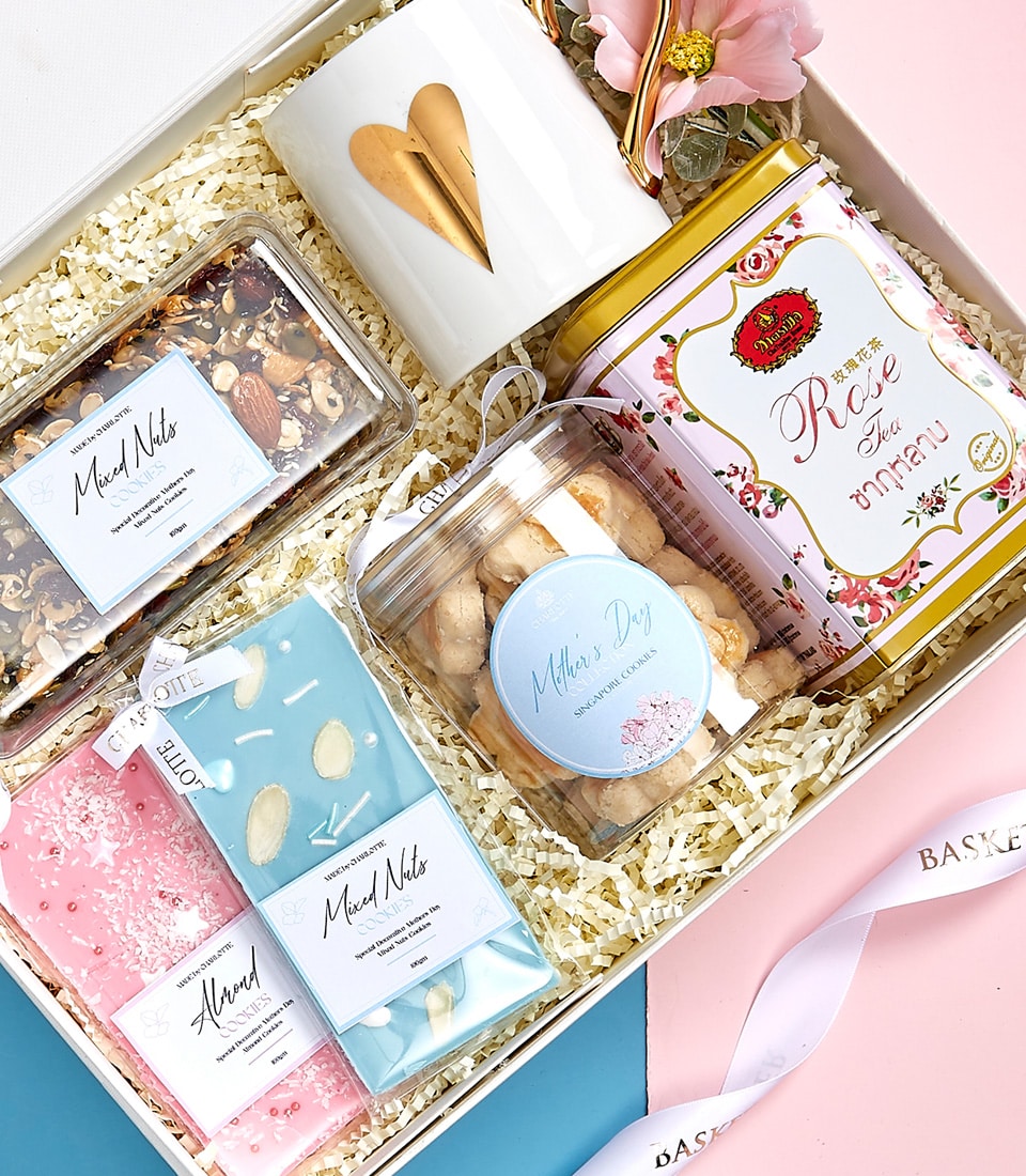 Elegant Mother's Day gift basket with gold heart mug, rose tea, gourmet cookies, and mixed nuts in pink and blue packaging