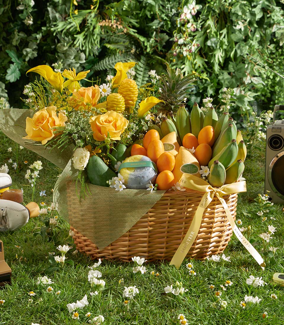 Golden tropical fruit and flower gift basket with roses, mangoes, and pineapple on wicker