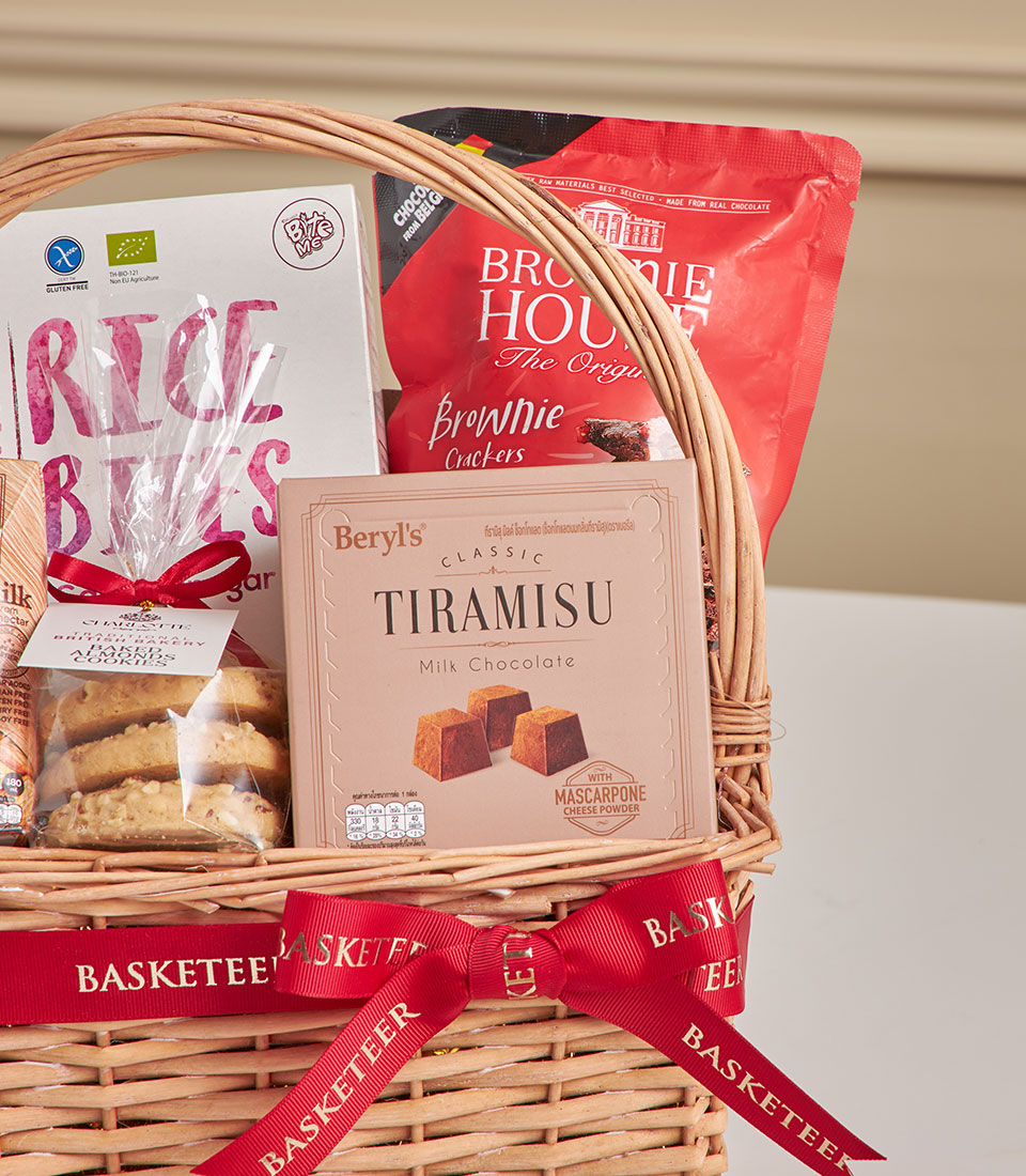 Woven wicker gift basket with tiramisu chocolate, almond cookies, and gourmet treats tied with red ribbon for New Year