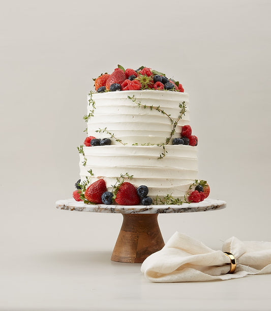 Two-tier white vanilla cake with fresh strawberries, raspberries, and blueberries on marble stand