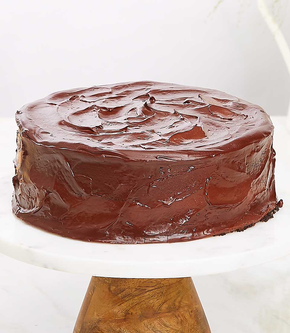 Dark chocolate ganache cake with glossy swirled frosting on white marble stand, perfect for chocolate lovers