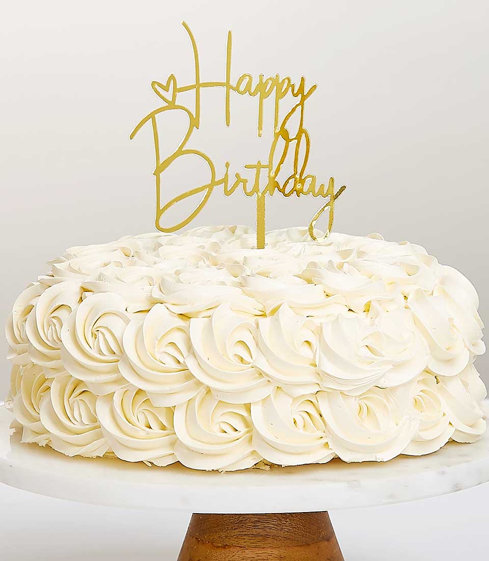 White buttercream birthday cake with gold Happy Birthday topper on marble stand