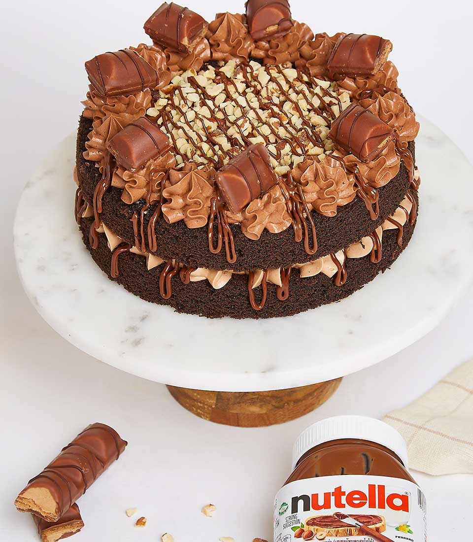 Two-tier chocolate cake with Nutella and Kinder Bueno, topped with chocolate drizzle and nuts on marble stand