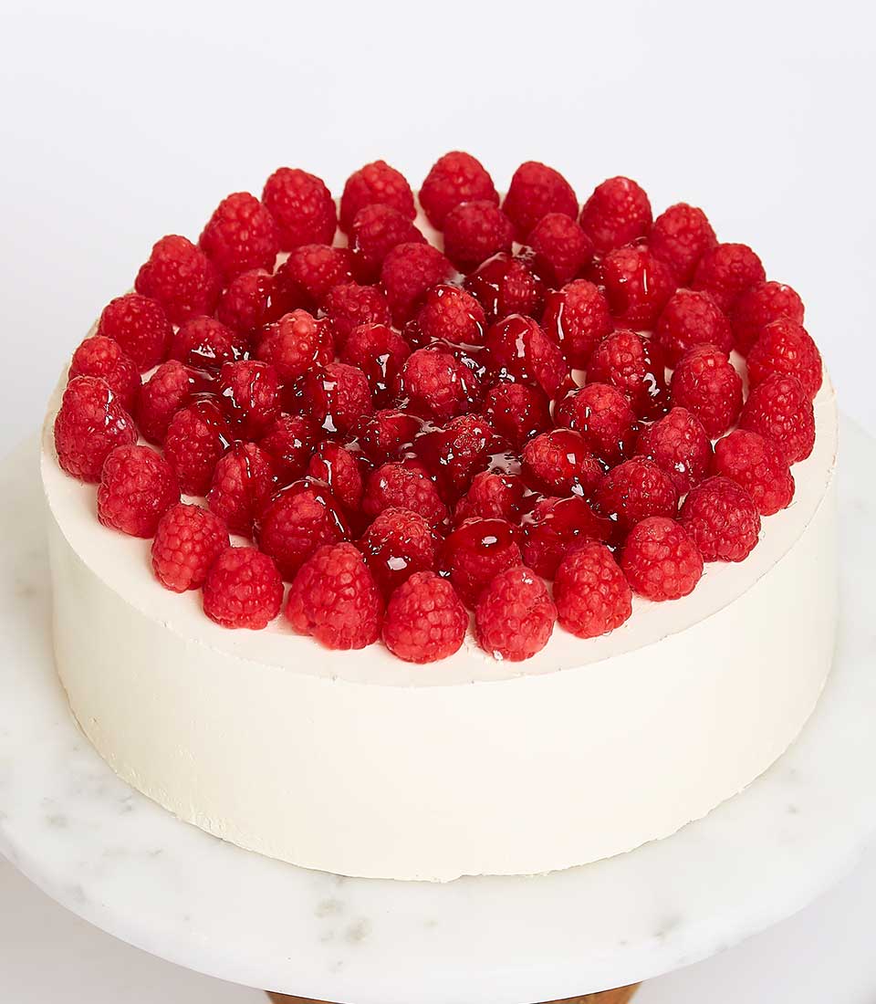 Luscious raspberry cake with white frosting and fresh red berries on marble stand