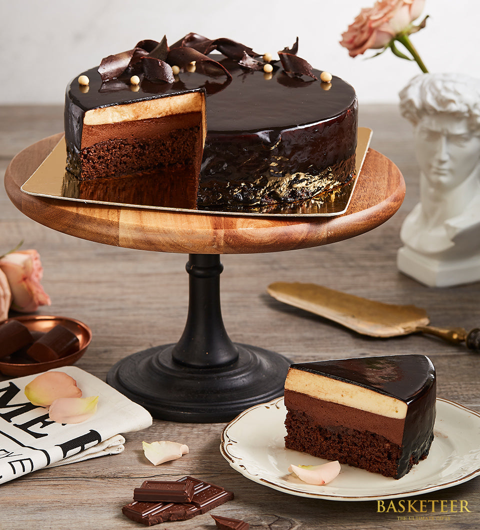 Rich layered chocolate cake with chocolate curls and edible pearls, displayed on wooden stand with slice plated