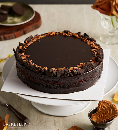 Decadent dark chocolate layer cake with glossy ganache and crushed cookie border on white cake stand, birthday celebration