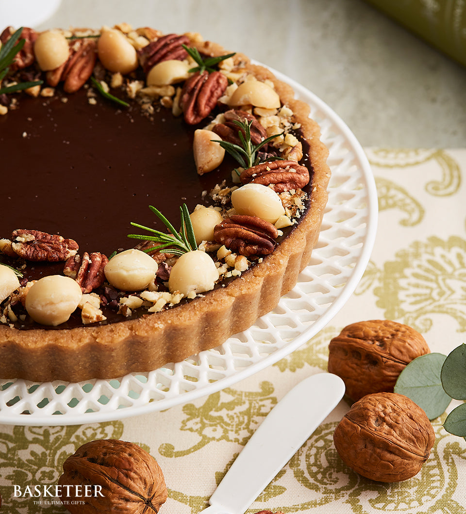 Dark chocolate tart with pecan and macadamia nut garnish on decorative cake stand, artisan birthday bakery gift