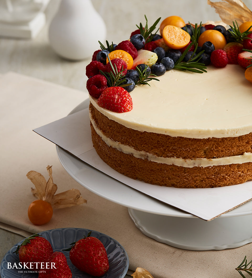 Mixed berry vanilla butter cake with fresh strawberries, blueberries, and rosemary on white frosting