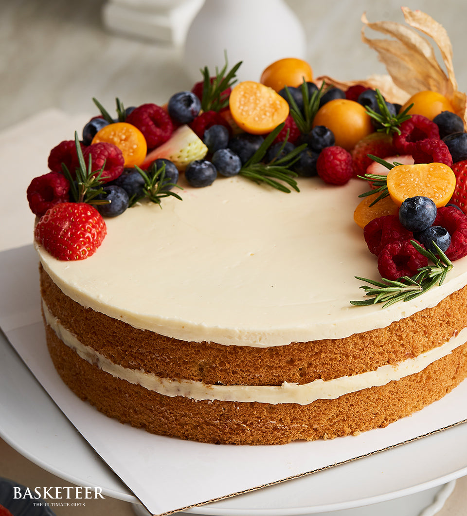 Naked vanilla butter cake with mixed fresh berries and rosemary on white frosting, birthday celebration cake