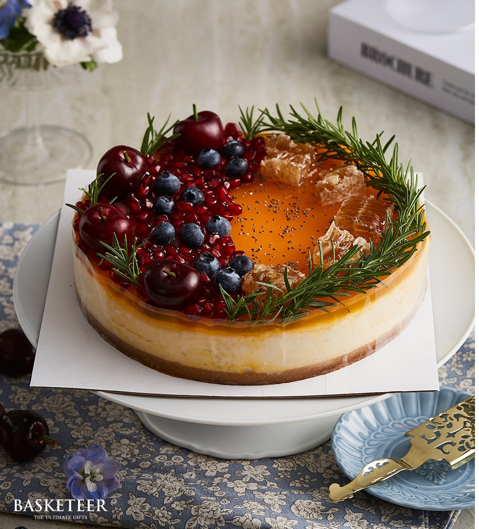 Berry honey cheesecake with fresh fruit, honeycomb, and rosemary on white cake stand